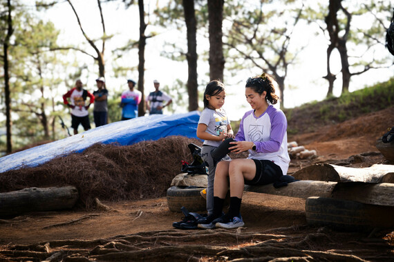 Samantha sits with a young girl on a bench in the forest